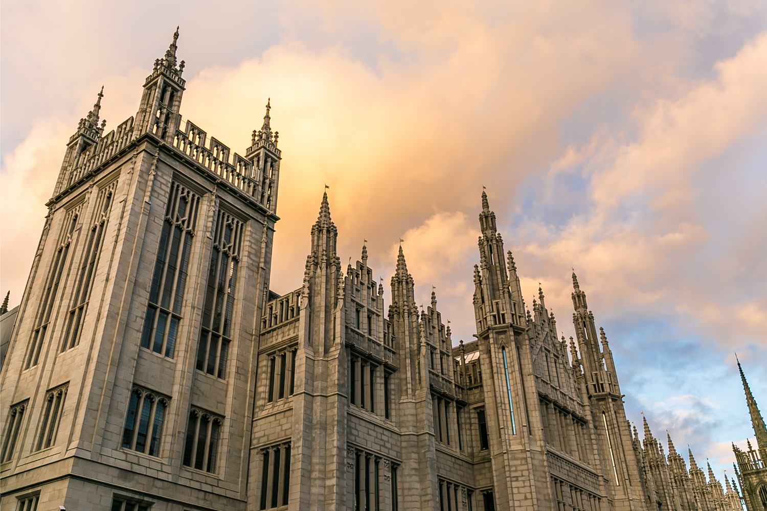 A view of Marischal College taken from a low angle and looking towards the sky. The roof parapets and architecture of this stone building are prominently featured.